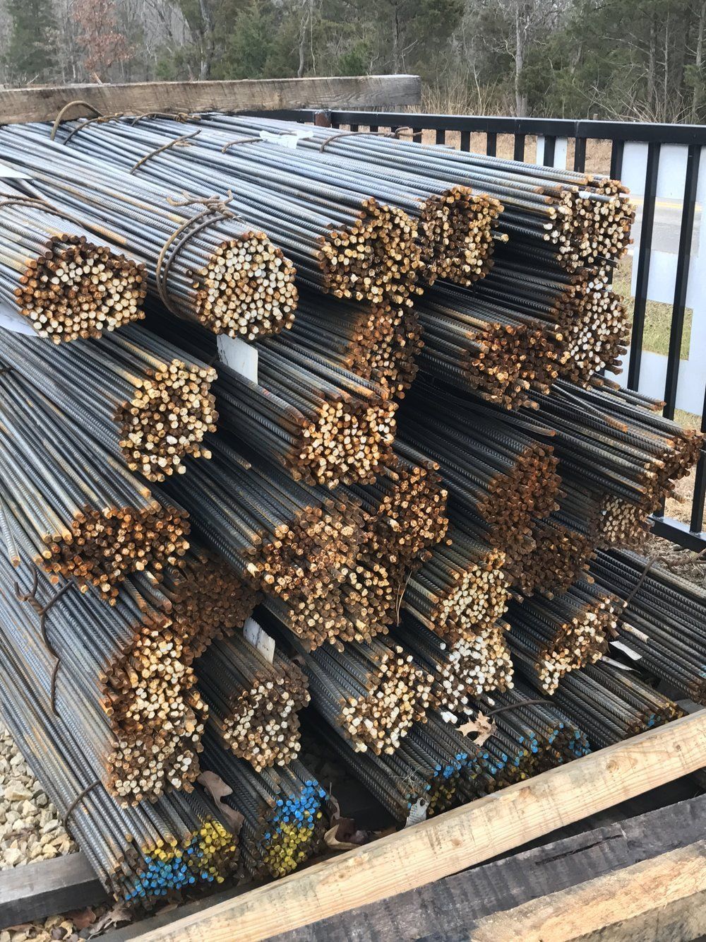 Stacked steel rebar bundles outdoors, with rusted ends and blue markings.