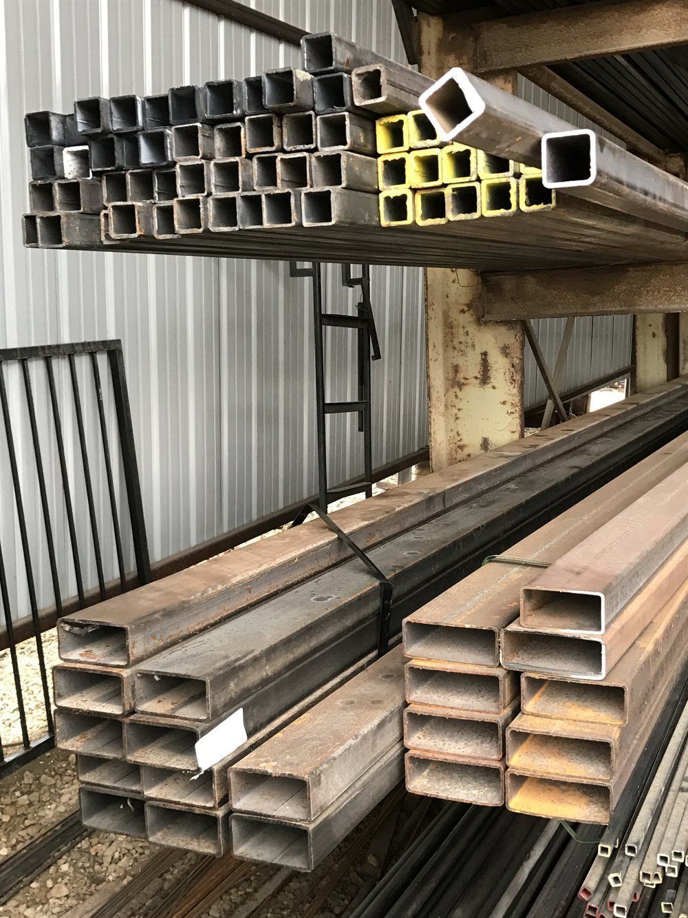 Stacks of rectangular metal tubes stored on industrial shelves in a warehouse.