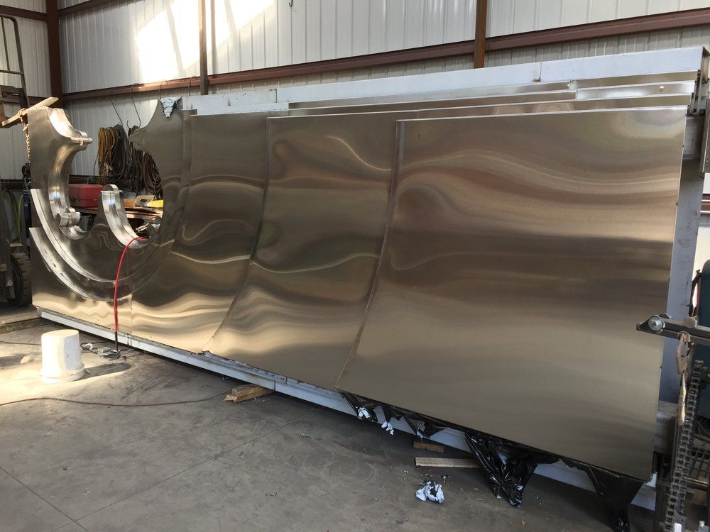 Large polished metal tank or trailer in a warehouse, with a circular opening at one end