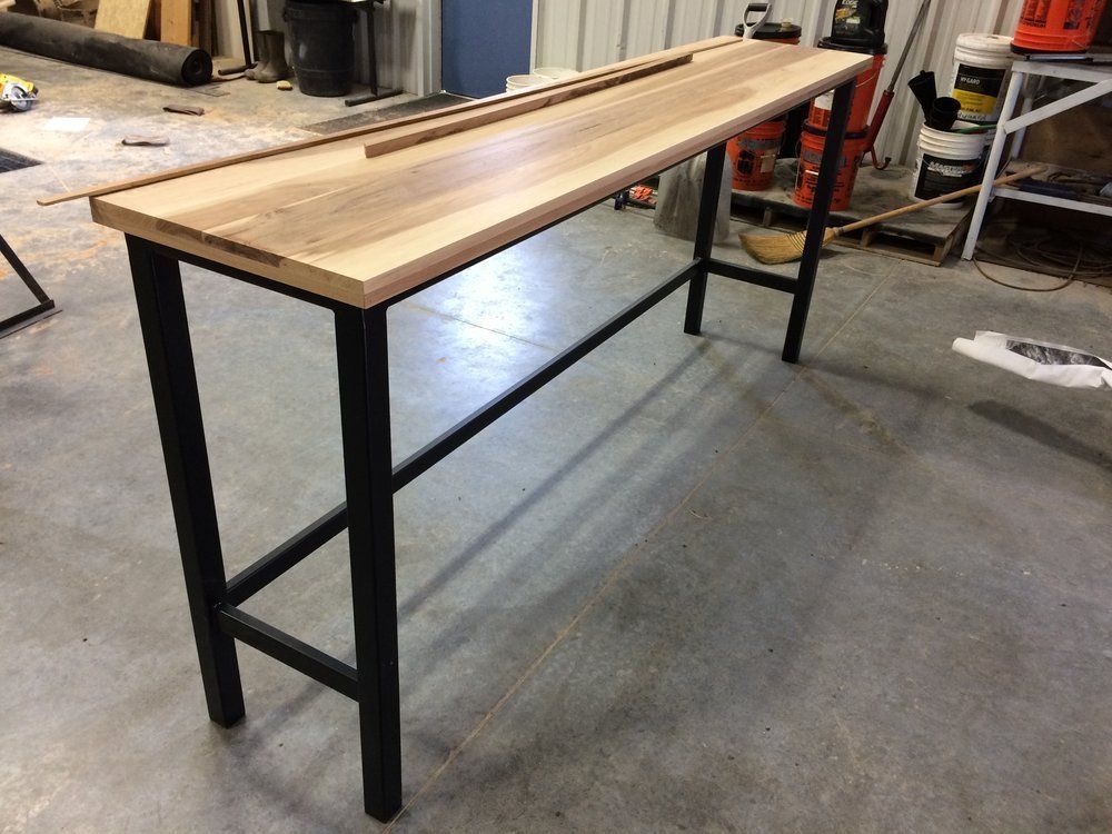 Long wooden workbench with black metal legs in a workshop garage.