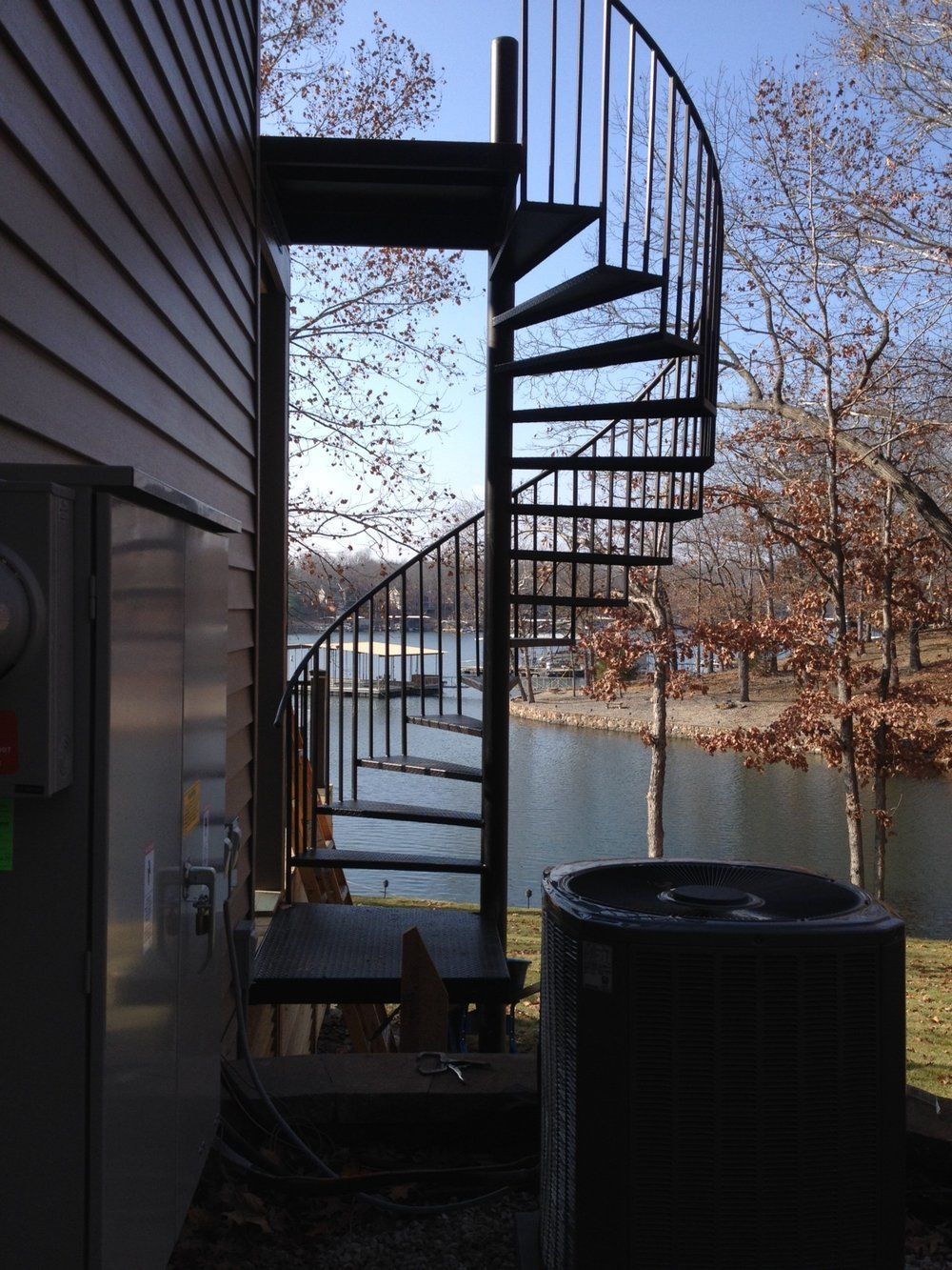 Outdoor metal spiral staircase beside a house, overlooking a lake with autumn trees.