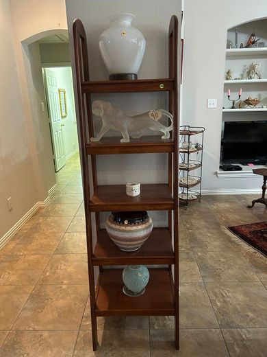 Tall wooden display shelf with decorative vases in a tiled living room, facing a TV area