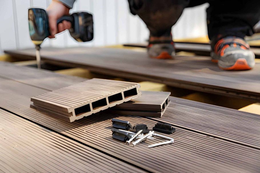 Close-up of a person installing deck boards with a drill and screws on a wooden deck.