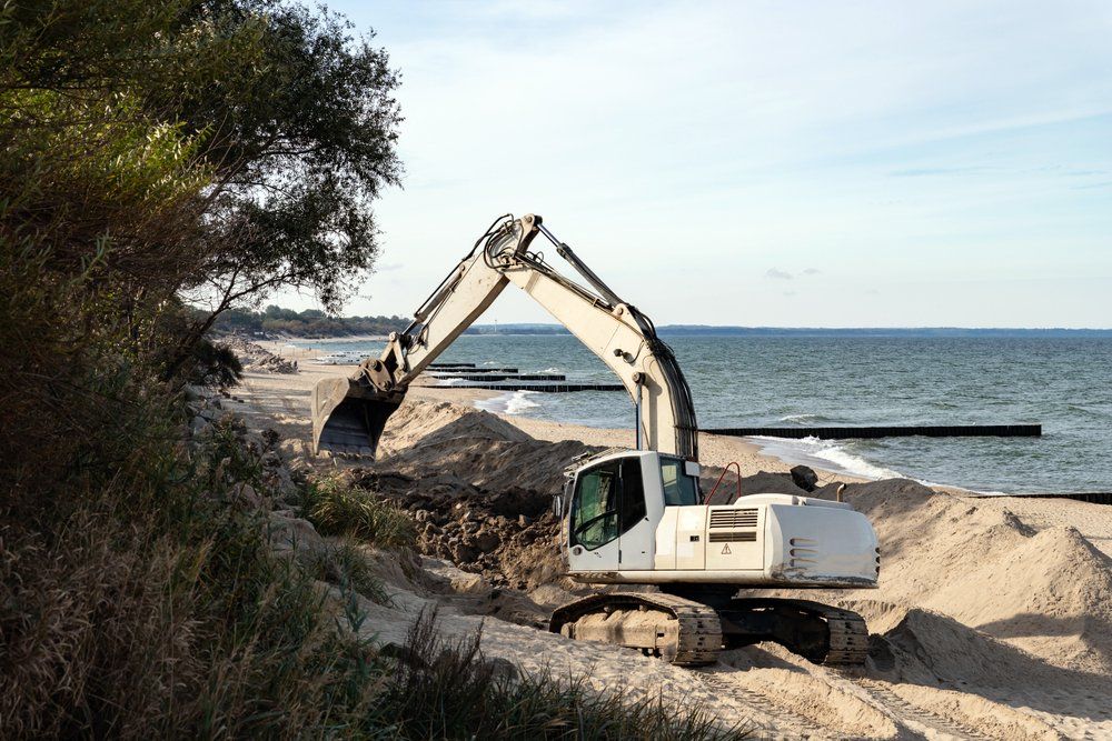 Une pelleteuse déplace du sable sur une plage, près de l'océan.
