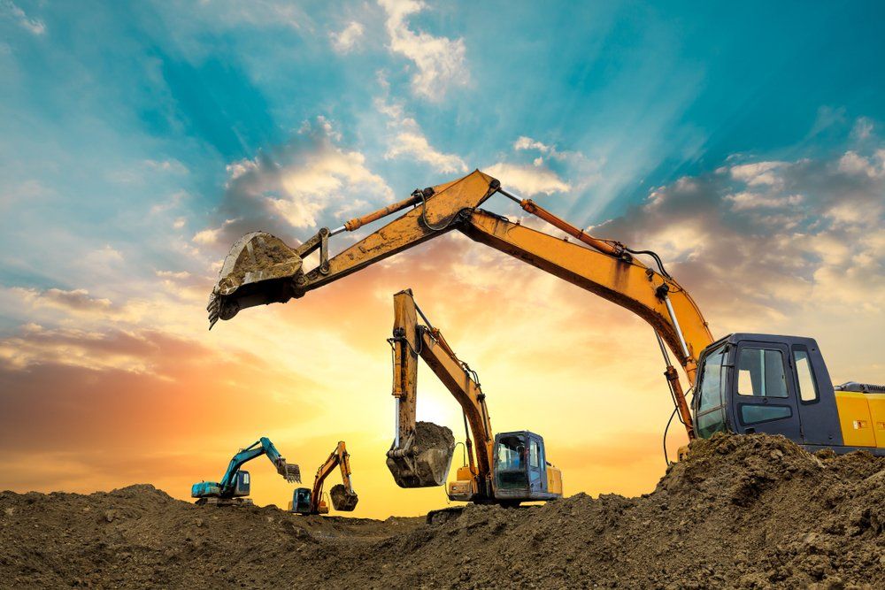 Des excavatrices sur un monticule de terre, excavant la terre sur fond de ciel couchant.