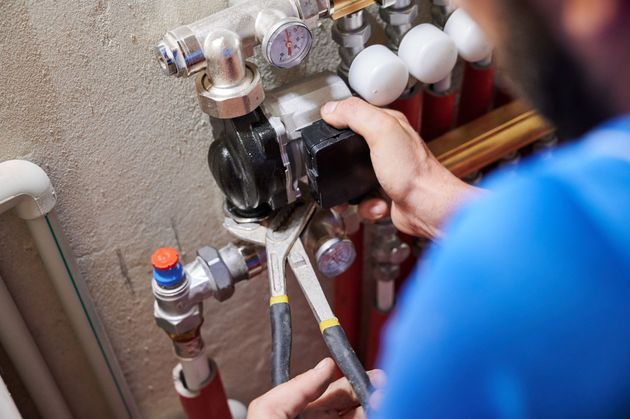 Plumber using pliers to work on pipes and valves.