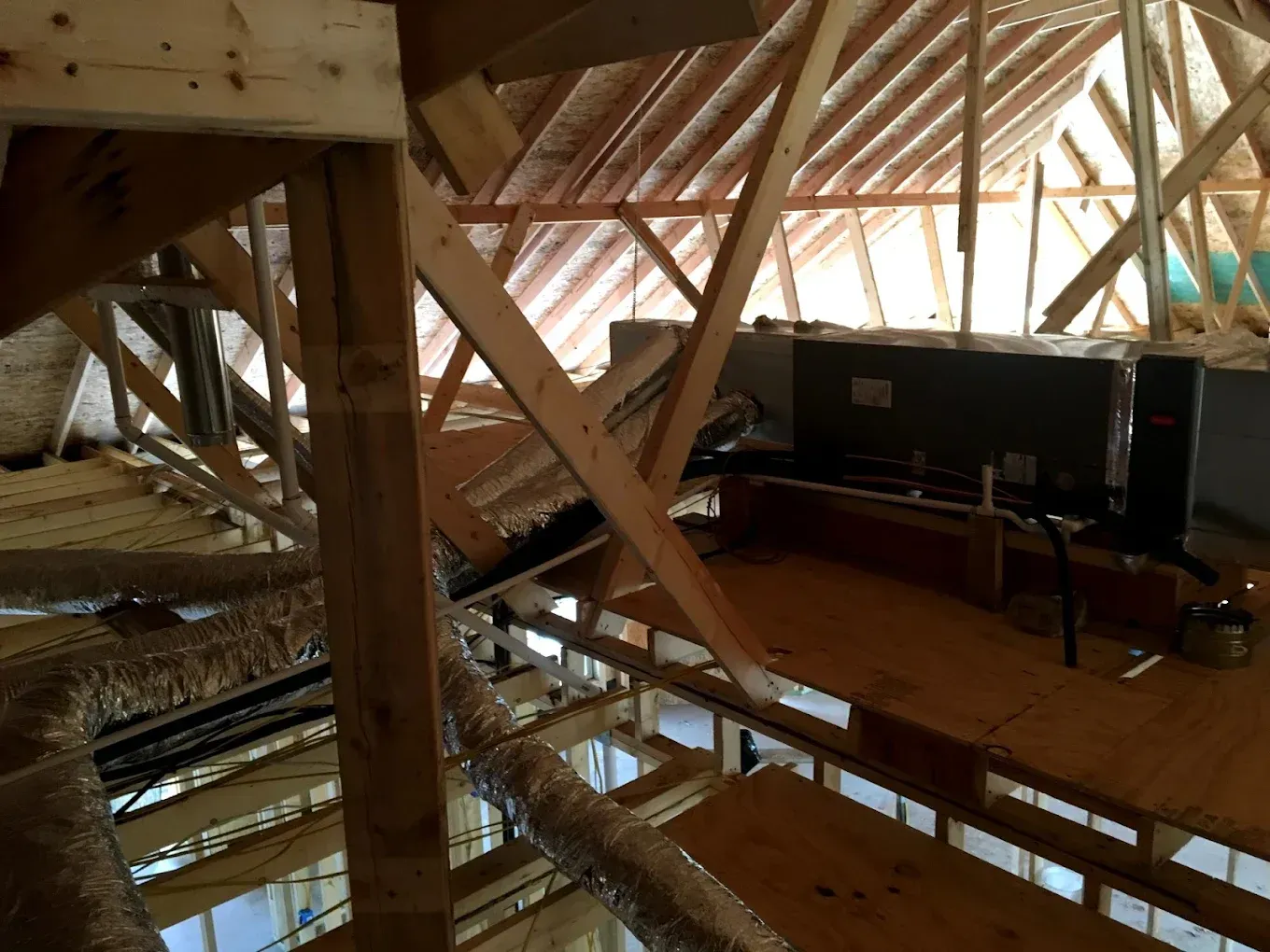 Interior attic with exposed wooden beams and a loft area with a desk and computer setup