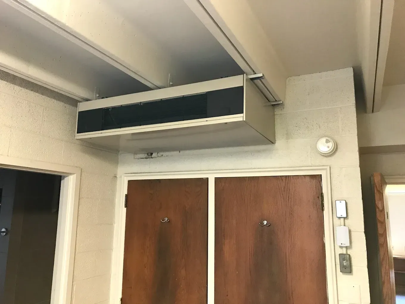 Indoor hallway with double wooden doors, overhead vent, and wall-mounted intercom panel