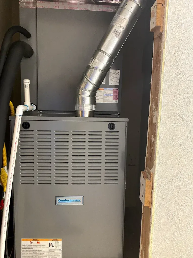 Gray furnace in a utility closet with a silver vent pipe and exposed insulation.