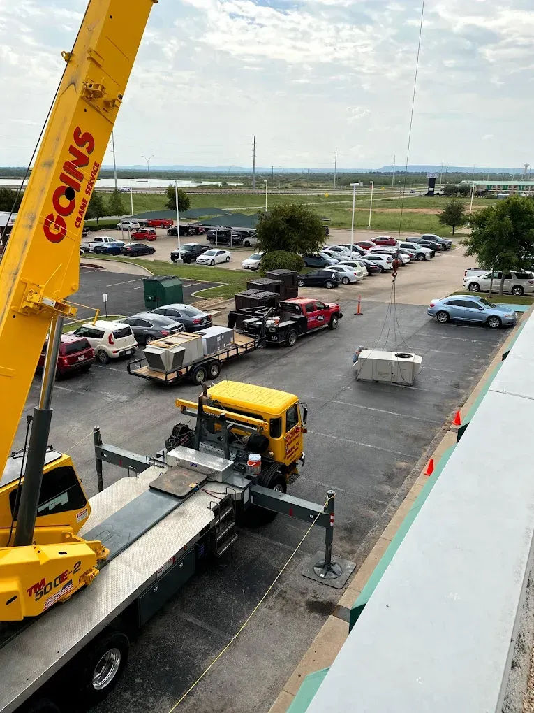 Crane lifting truck in a busy parking lot near a road and open field