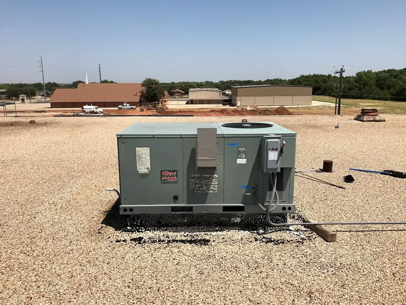 Gray industrial generator on gravel in a sunny open lot, with buildings and trees in the background
