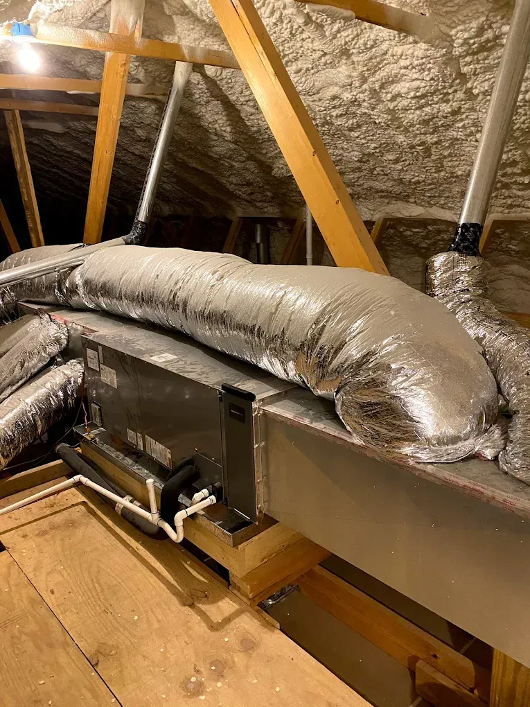 Foil-insulated HVAC ducts in an attic with wooden rafters and a metal air handler