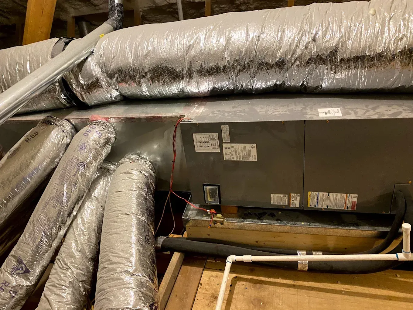 Insulated HVAC ducts and equipment in a mechanical room, with exposed wiring and labels on a metal unit.