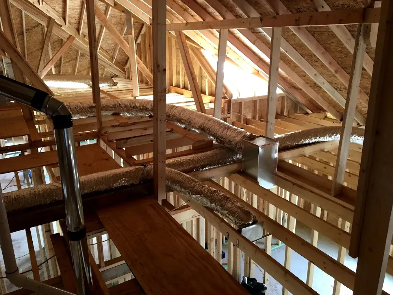 Wooden attic framing with exposed beams, trusses, and a metal duct in a partially finished roof space