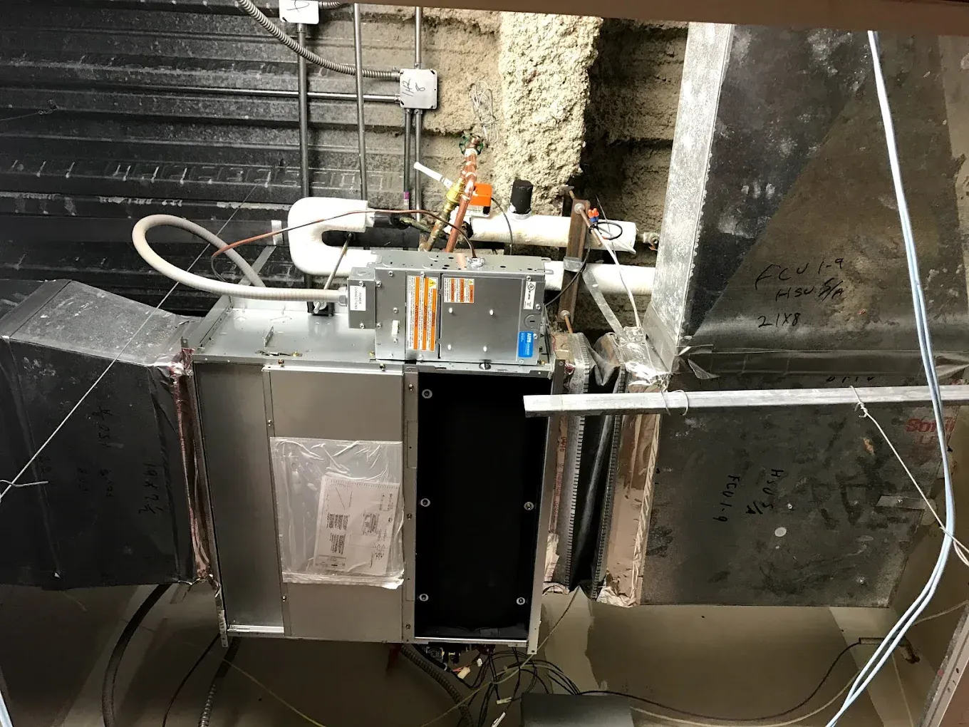 Industrial HVAC equipment with exposed wiring and pipes in a utility room