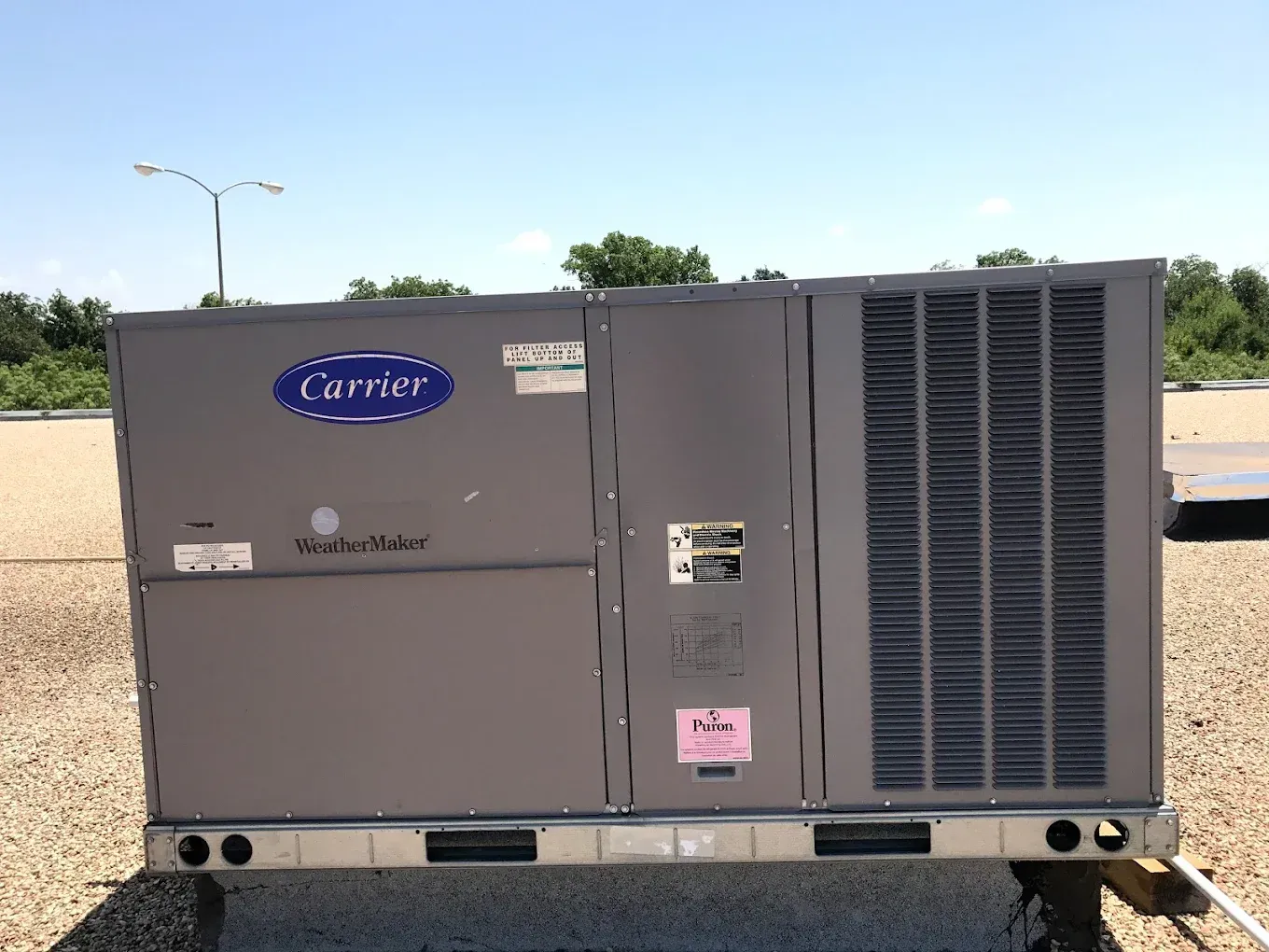 Gray Carrier rooftop HVAC unit with large front vent and label stickers outdoors against blue sky.