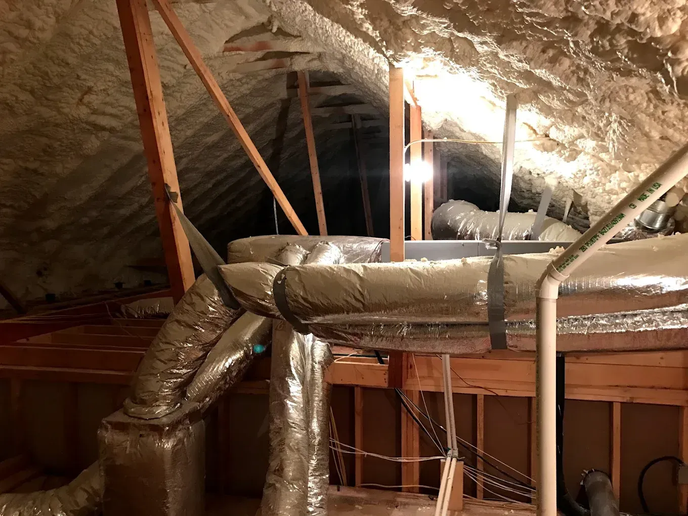 Attic HVAC ducts with silver insulation, wooden framing, and a large vent opening
