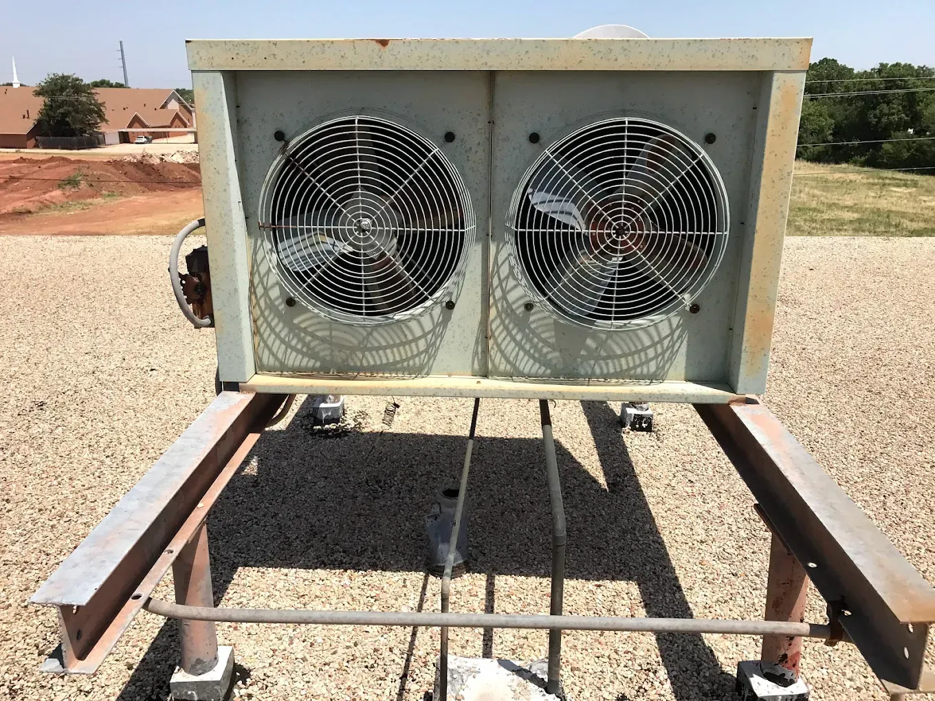 Two large fans mounted in a metal unit on a trailer in a gravel lot.