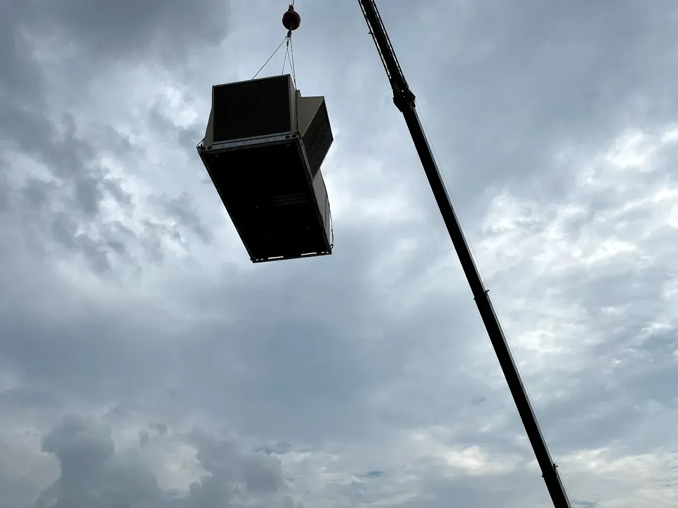 Suspended black speaker hoisted by a crane against a cloudy sky