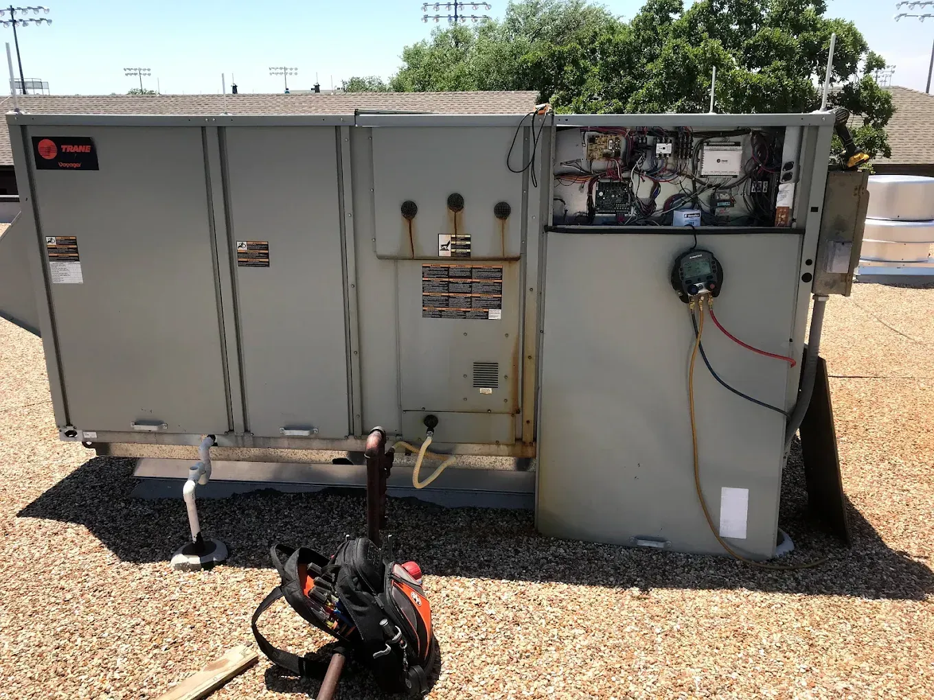 Large gray electrical equipment cabinet outdoors on gravel, with exposed wiring and a detached panel.