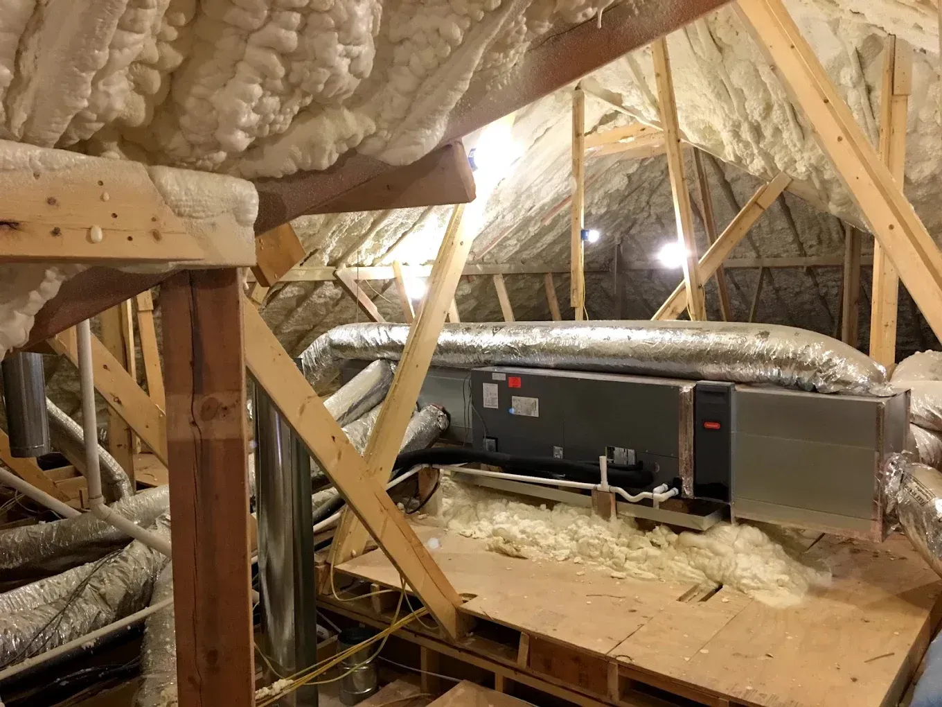 Attic HVAC unit amid exposed insulation and wooden rafters