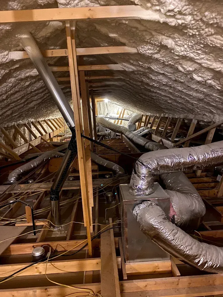 Insulated attic with exposed wooden beams and ductwork, showing attic framing and ventilation system
