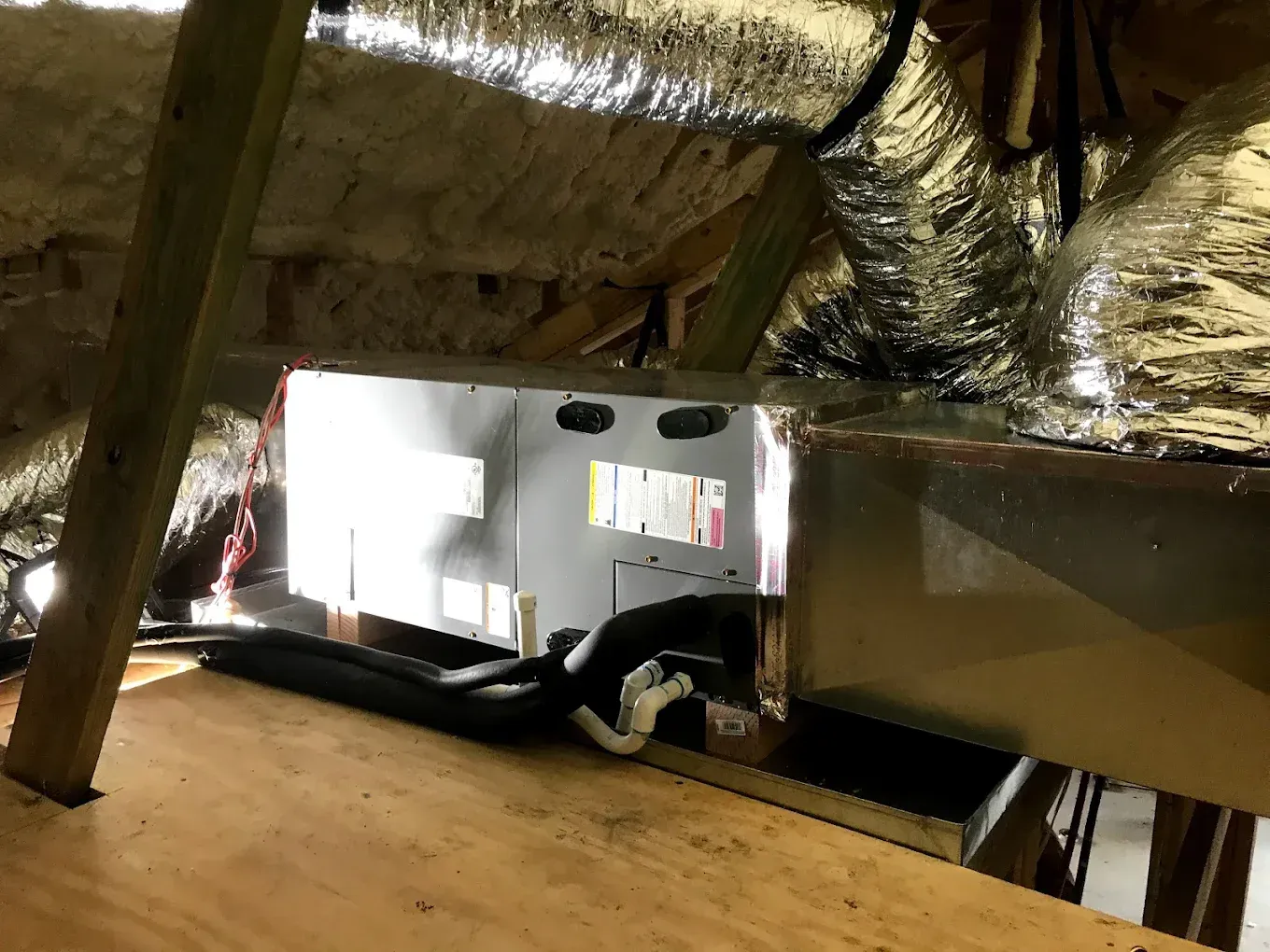 Attic space with insulation, ductwork, and a mounted HVAC unit under a sloped roof