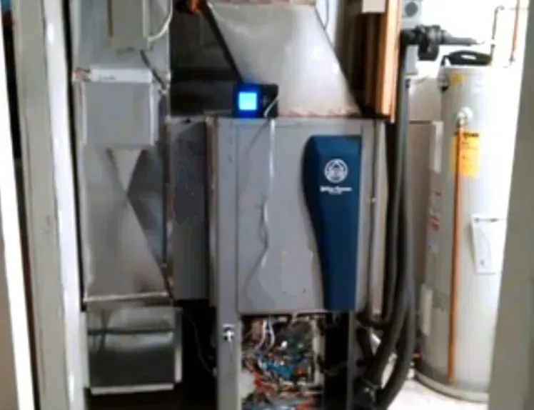 HVAC furnace with open access panel and visible wiring beside a water heater in a utility room