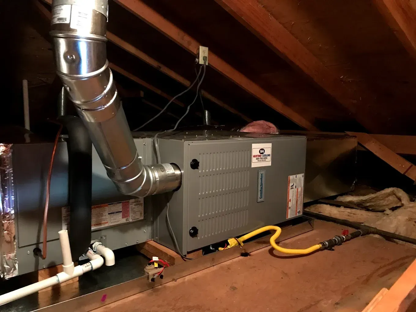 Attic HVAC unit with ductwork, pipes, and electrical wiring under a sloped roof