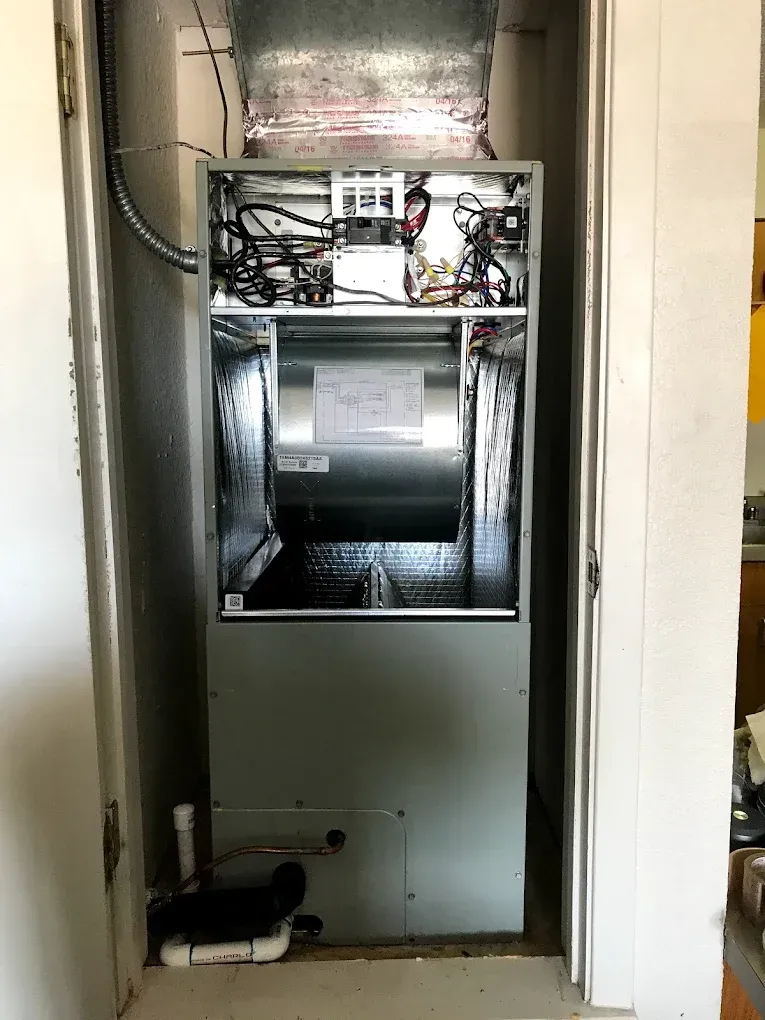 Open electrical cabinet with wiring, a large metal drum, and pipes inside a utility closet