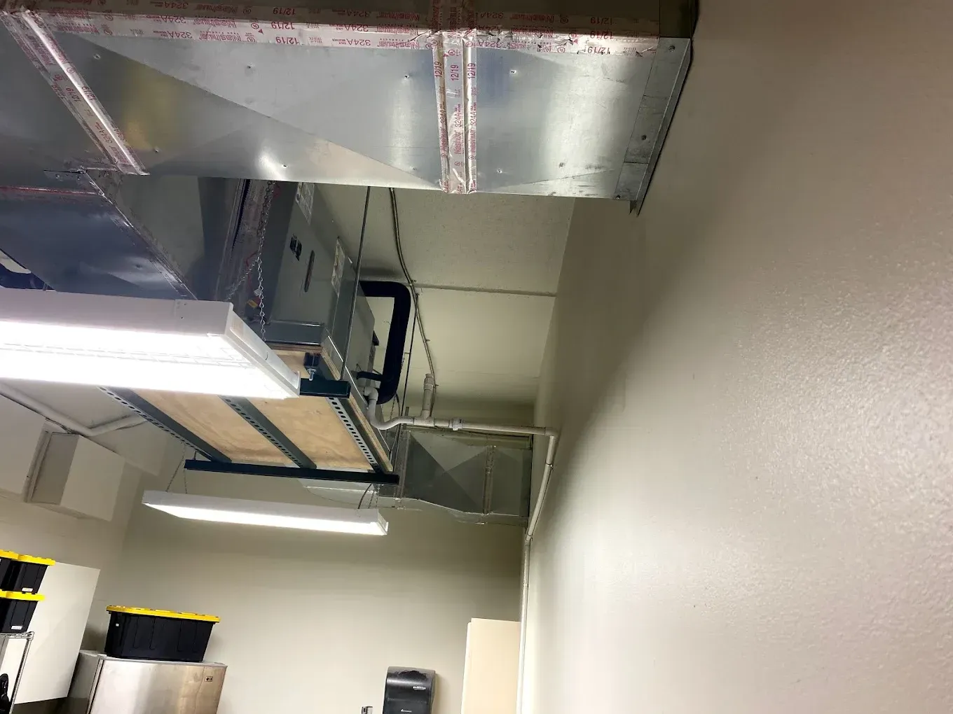 Industrial ceiling with exposed metal ductwork and fluorescent lights in a room under construction
