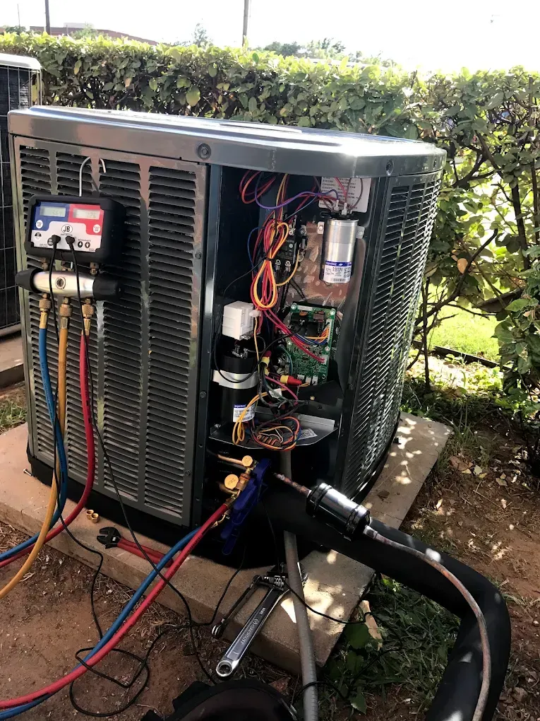 Outdoor HVAC unit with the side panel open, showing wiring and gauges connected for service.