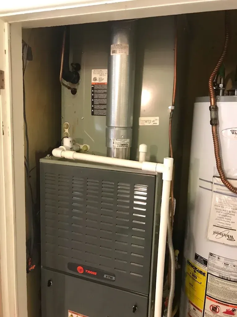 Residential furnace and water heater in a utility closet, with exposed pipes and ductwork.