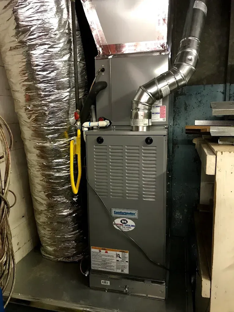 Gas furnace in a basement with silver ducts and a yellow service switch next to it