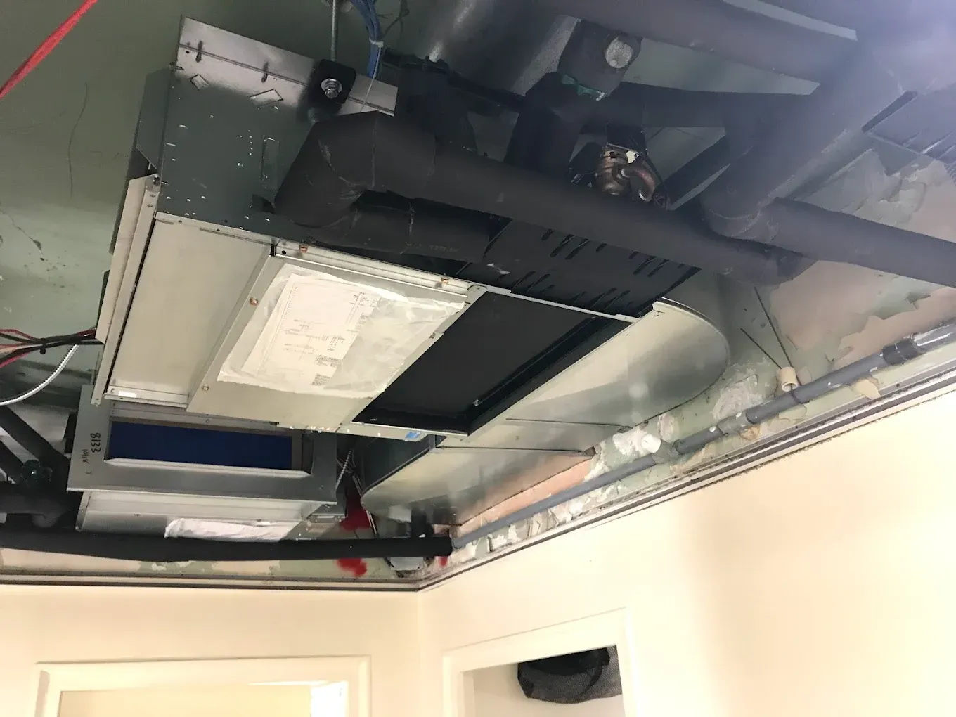Ceiling-mounted HVAC unit and exposed ductwork in a room with white walls.