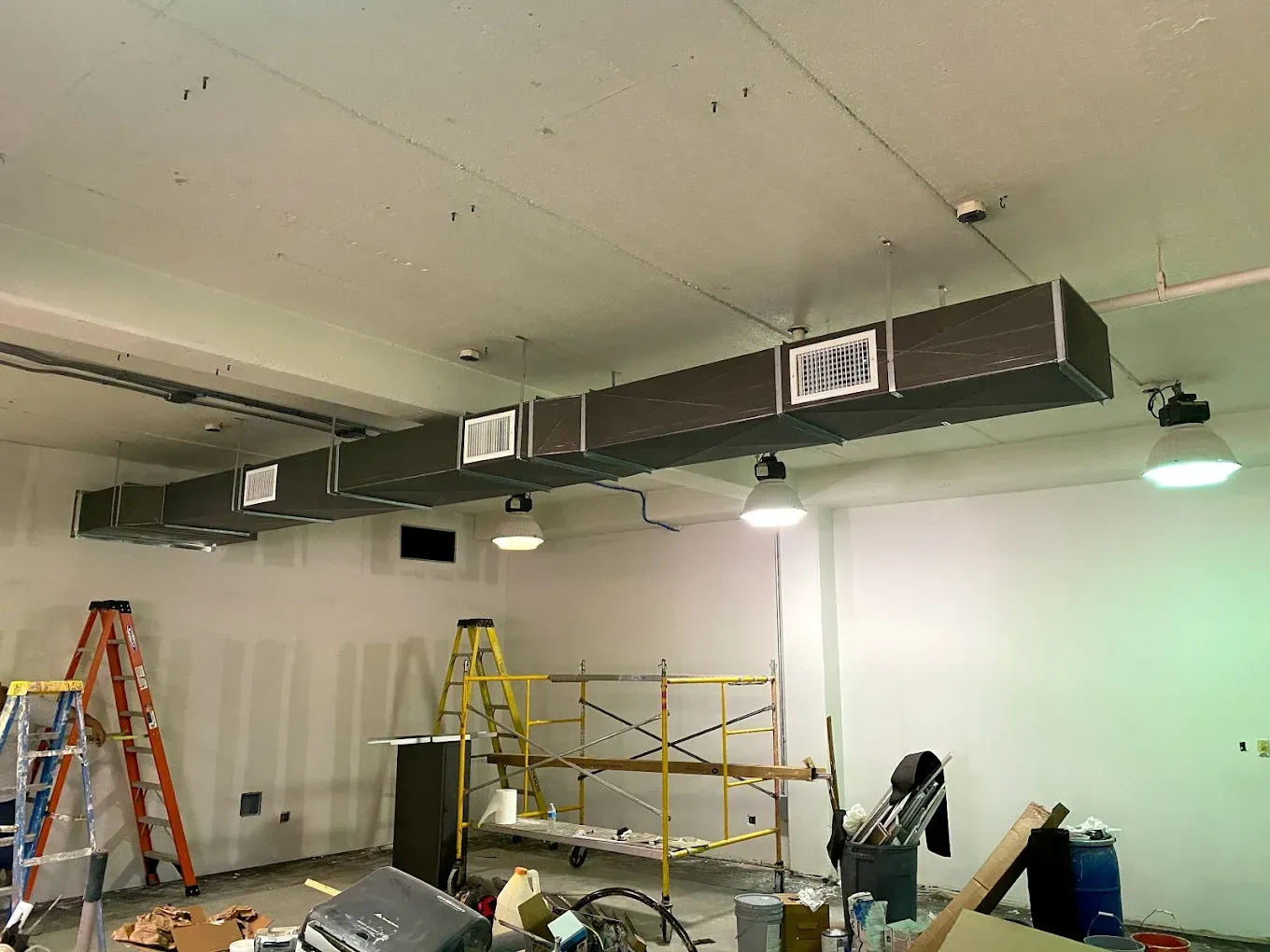 Empty room under renovation with ladders, scaffolding, and ceiling ducts.