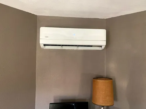 White wall-mounted air conditioner above a lamp in a beige room