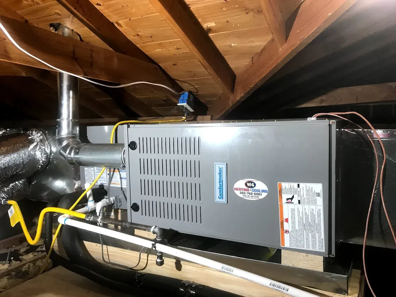 Furnace and ductwork in a crawlspace under exposed wooden beams, with metal venting and yellow gas line.