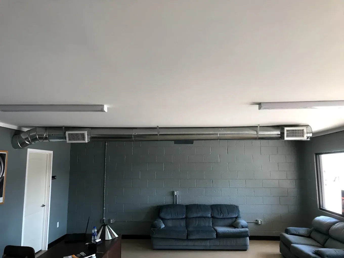 Sparse lounge with dark sofas against a black brick wall and bright windows.