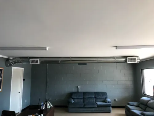 Industrial-style room with dark gray walls, two black sofas, and fluorescent ceiling lights