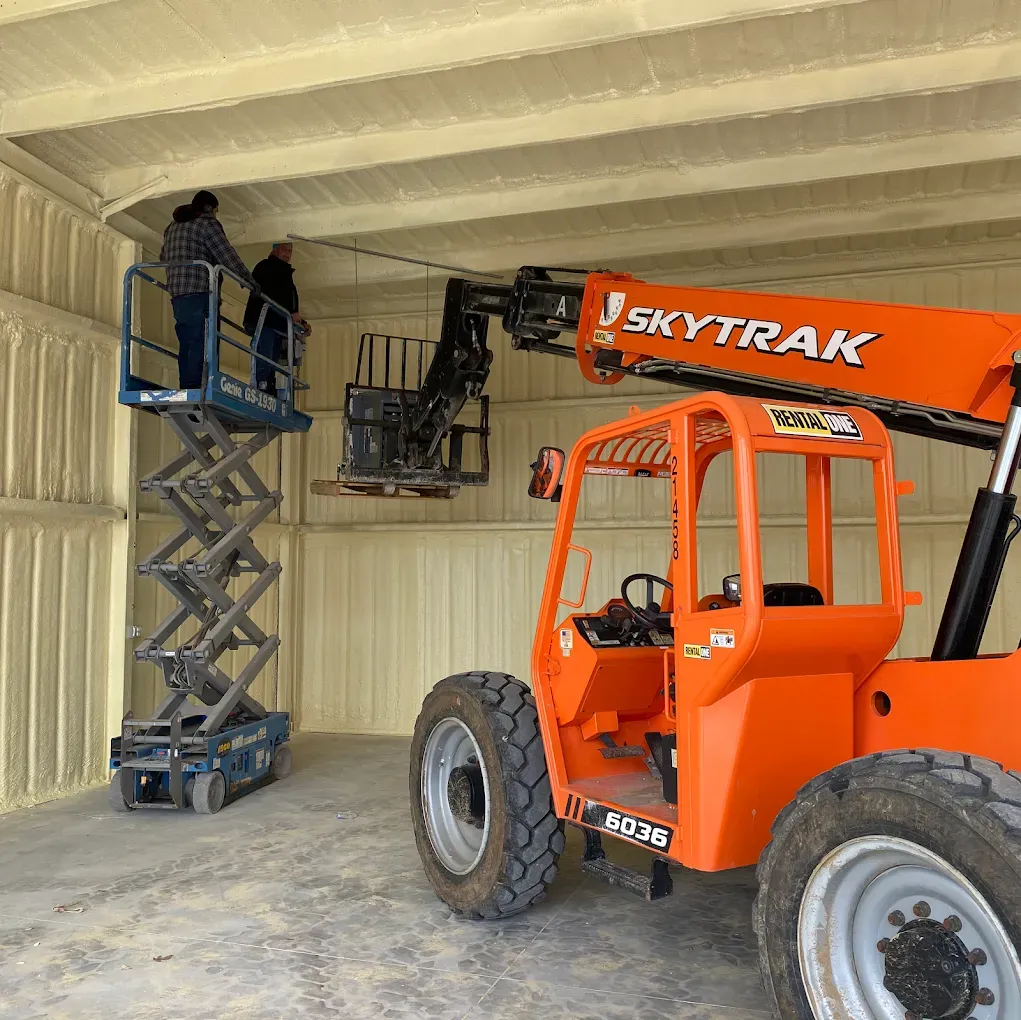 Orange Skytrak forklift inside a metal shed, next to a blue scissor lift and a raised work platform.