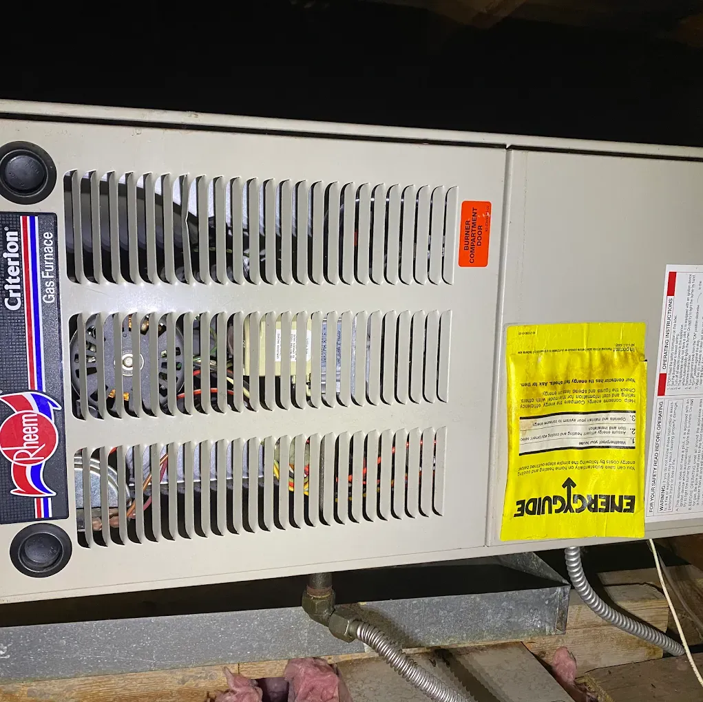 Front of a beige furnace or HVAC unit with vents, labels, and wiring visible on the floor.