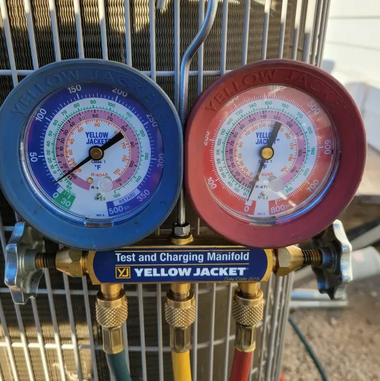 Blue and red HVAC manifold gauge set with pressure dials and brass fittings on a yellow jacket tool board