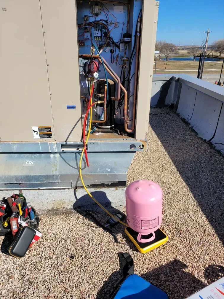 HVAC unit on rooftop with open panel, tools, and a pink refrigerant cylinder nearby