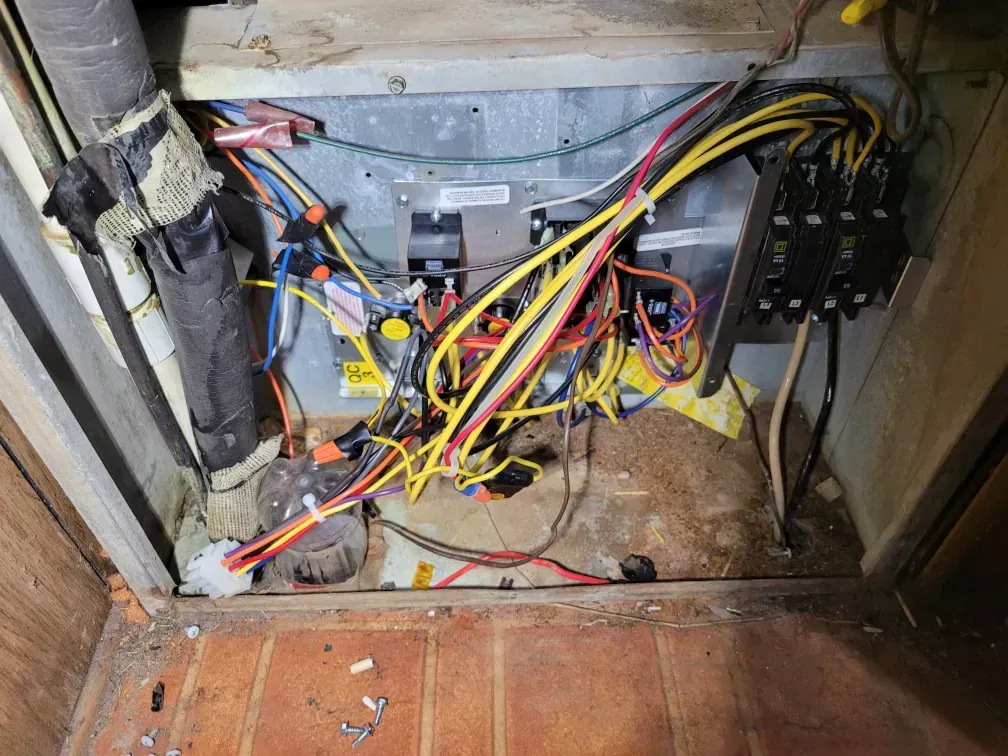 Messy electrical wiring and components inside a cabinet, with red, yellow, and black cables tangled across the floor.