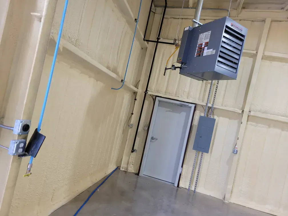 Industrial room with tan walls, overhead heater, gray door, and electrical conduit along the wall.