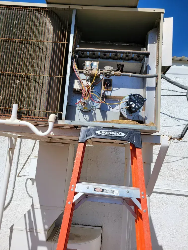 Open HVAC unit on a wall with a red ladder leaning below it