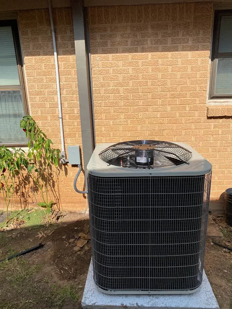Outdoor air conditioner unit beside a brick house wall on a concrete pad