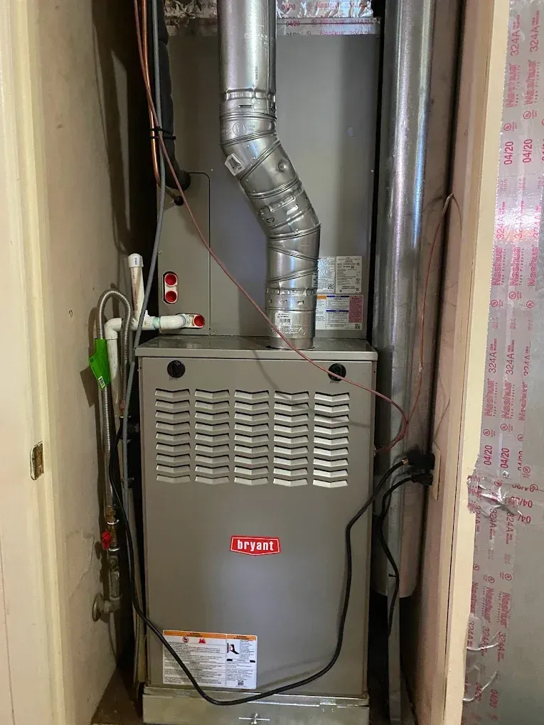 Furnace unit in a narrow utility closet with silver ductwork and visible wires.