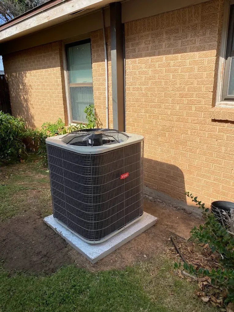 Outdoor air conditioner unit beside a tan brick house on a concrete pad